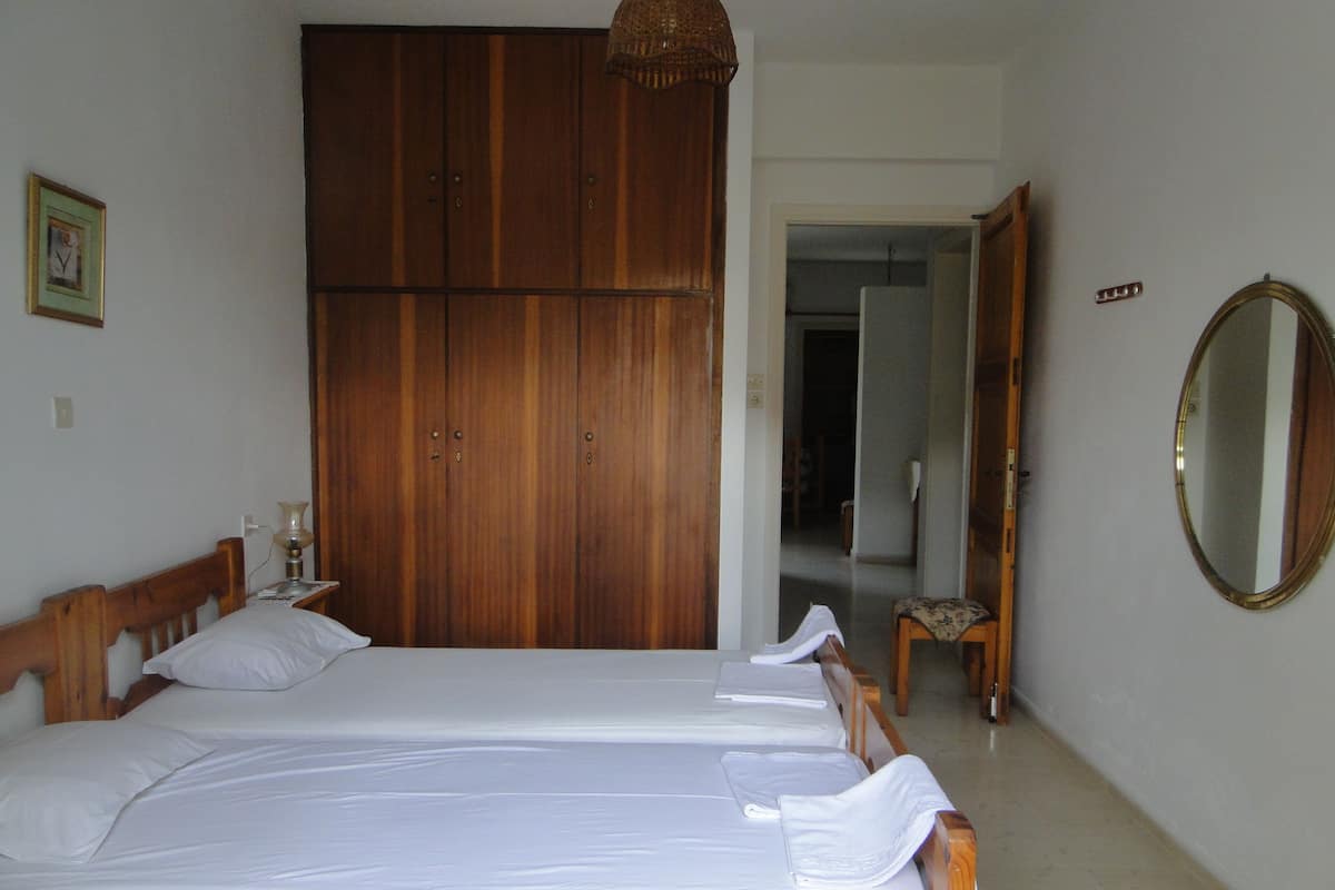 A bedroom with two single beds, a wooden wardrobe, a mirror, and a small table with a lamp.