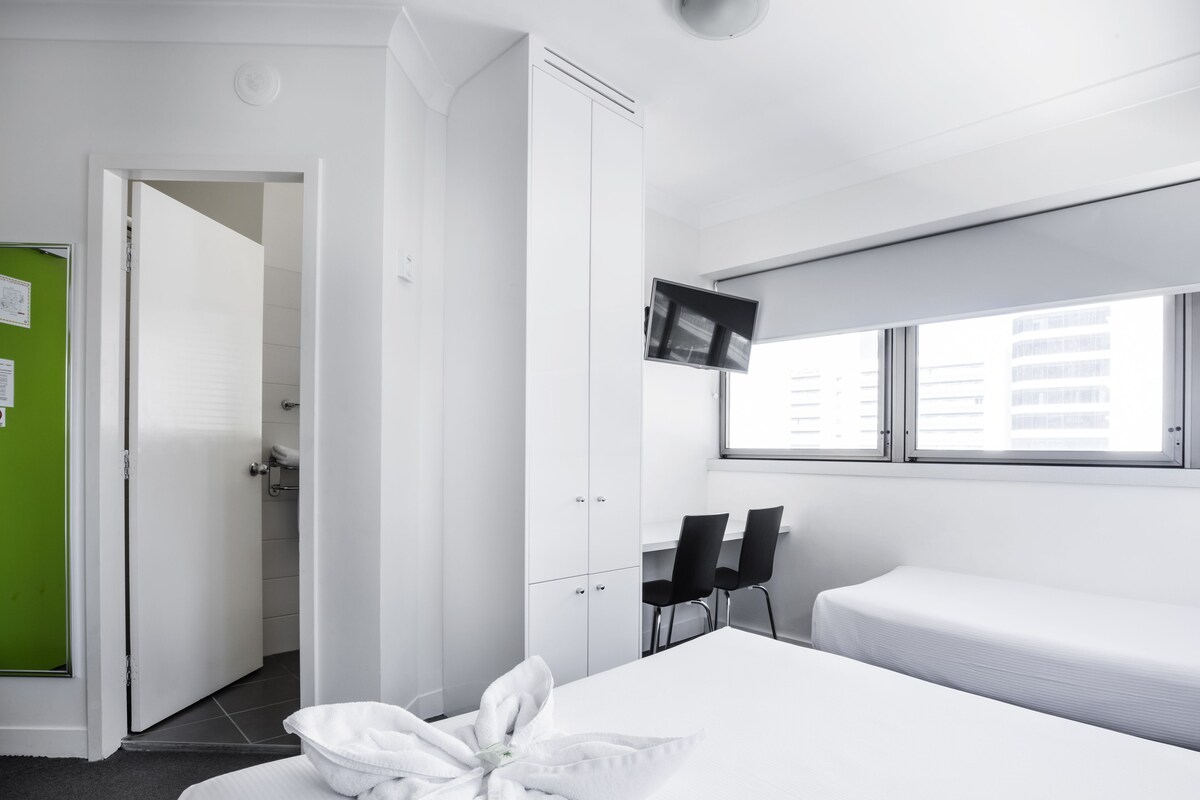 A hotel room with a bed, a desk, two chairs, a TV, and a window.