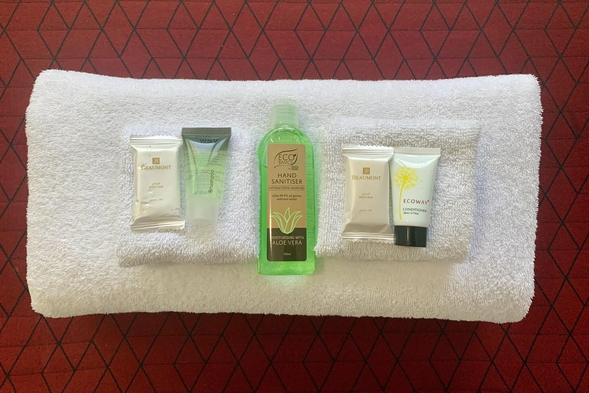 A white towel with five personal care items: two body bars, a hand sanitizer, a conditioner, and a shampoo.