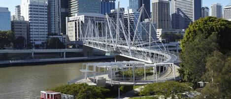 A modern bridge with a unique lattice structure spanning over a river, surrounded by urban buildings.