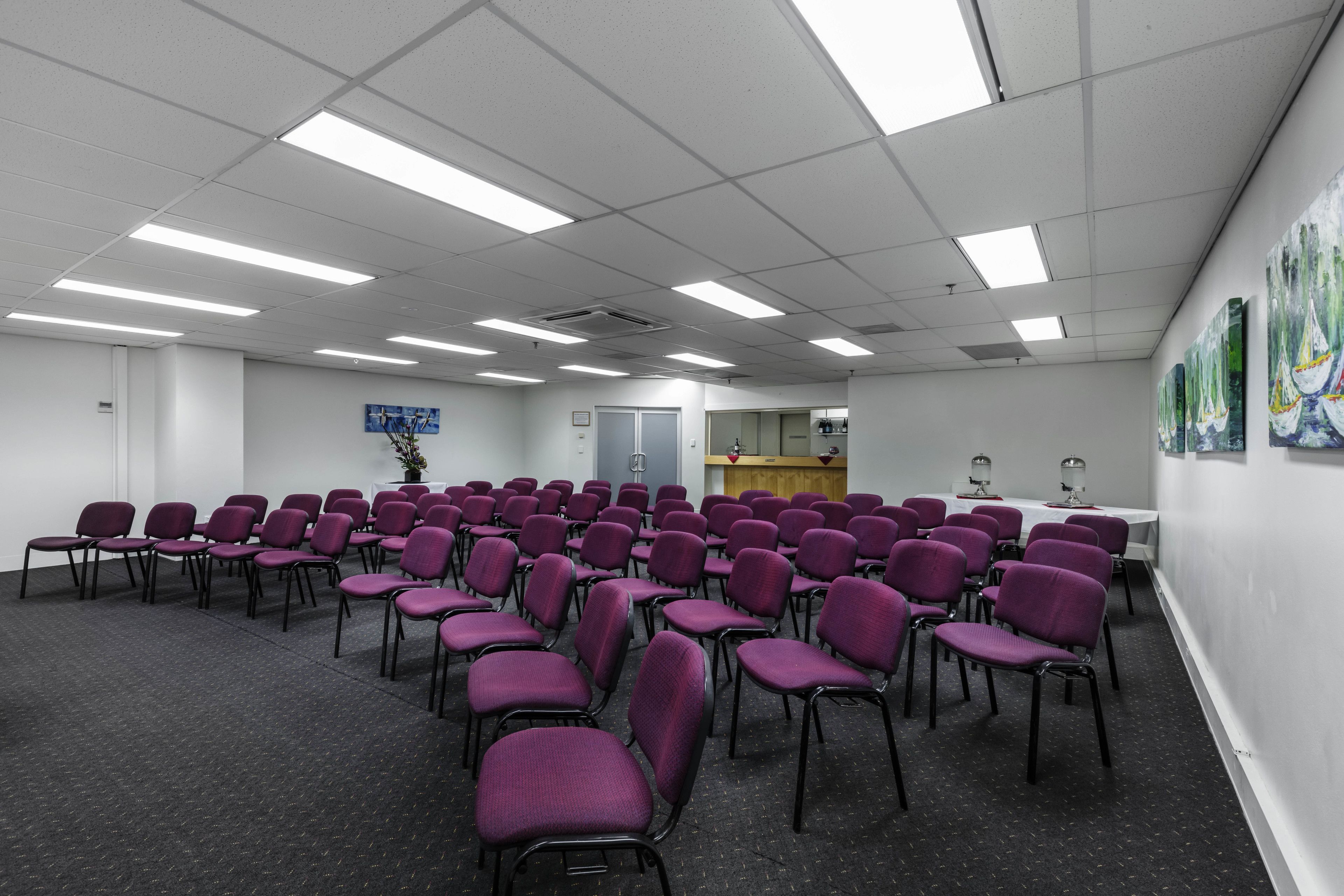 A conference room with rows of purple chairs, a white table, and a wooden podium.