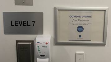 Pared con un aviso enmarcado sobre la actualización del COVID-19, dispensador de gel hidroalcohólico, detector de incendios y señal de indicador de nivel.