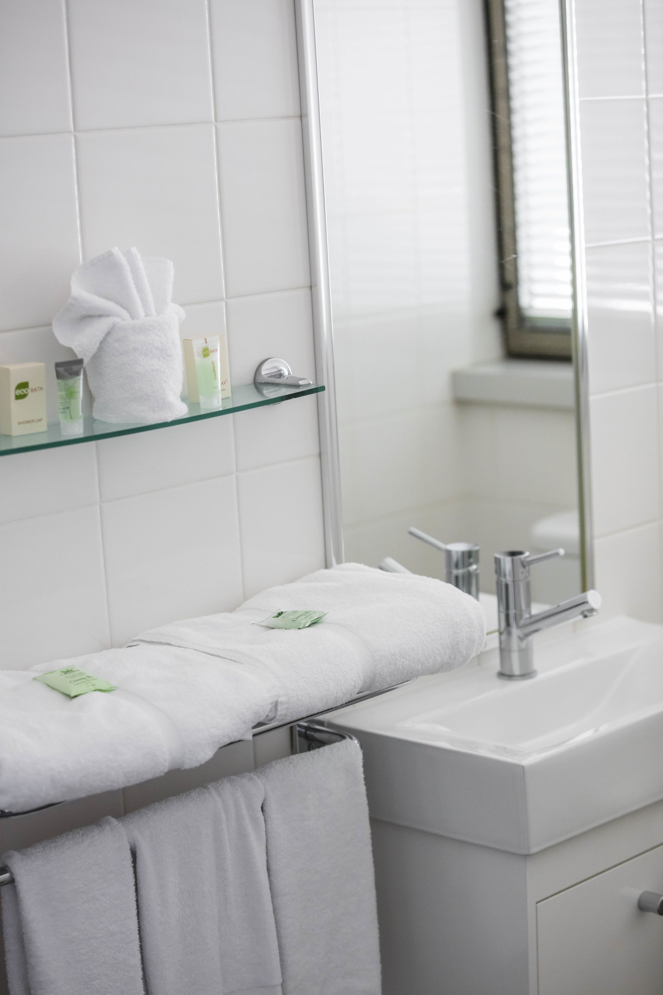 Une salle de bain moderne avec une étagère en verre où sont rangés les articles de toilette, un lavabo blanc et un miroir.