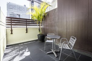 A balcony with a potted plant, two metal chairs, and a small round table.