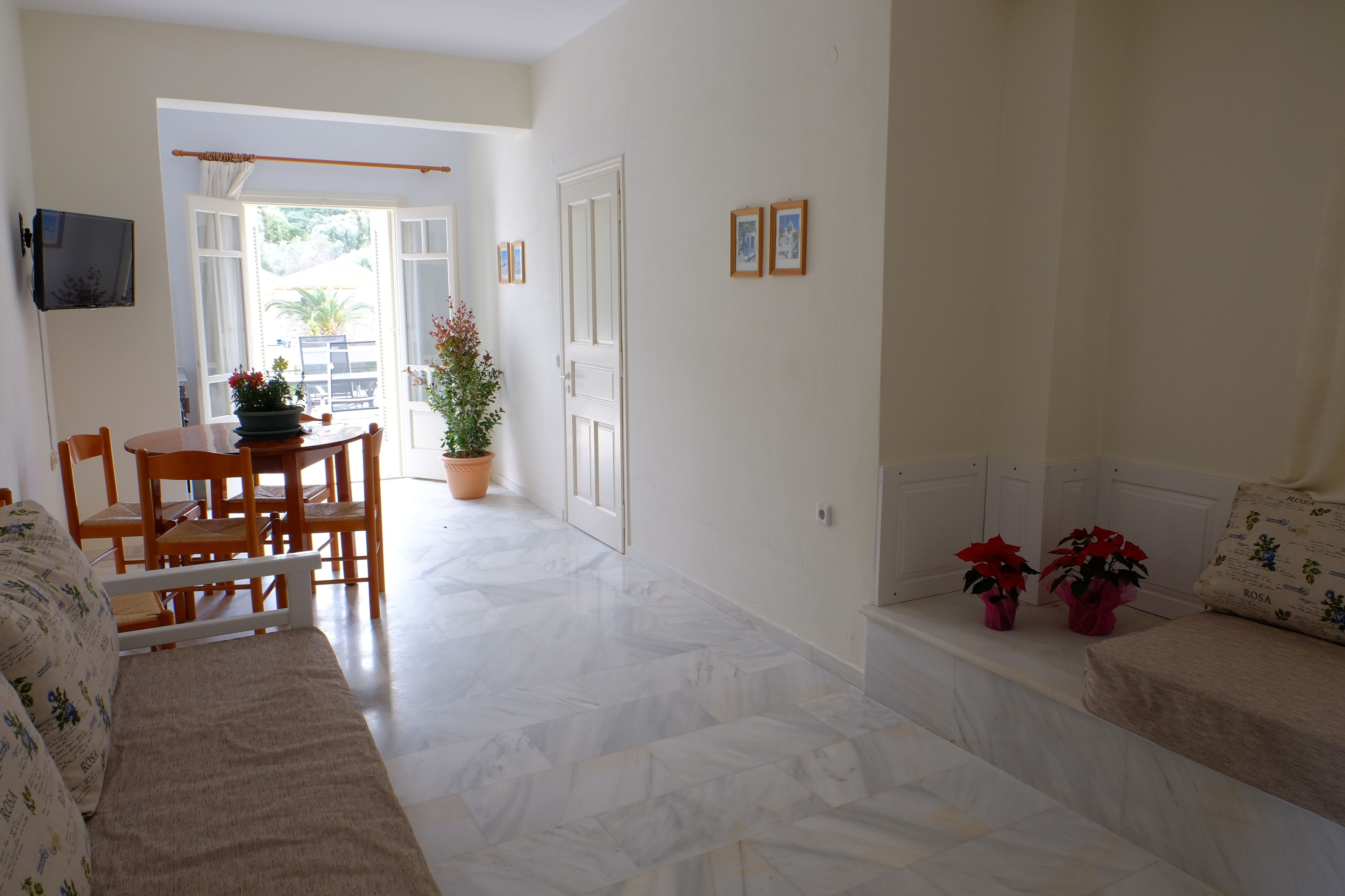 A spacious living area with a sofa, a dining table with chairs, a potted plant, and a bench with red flowers.