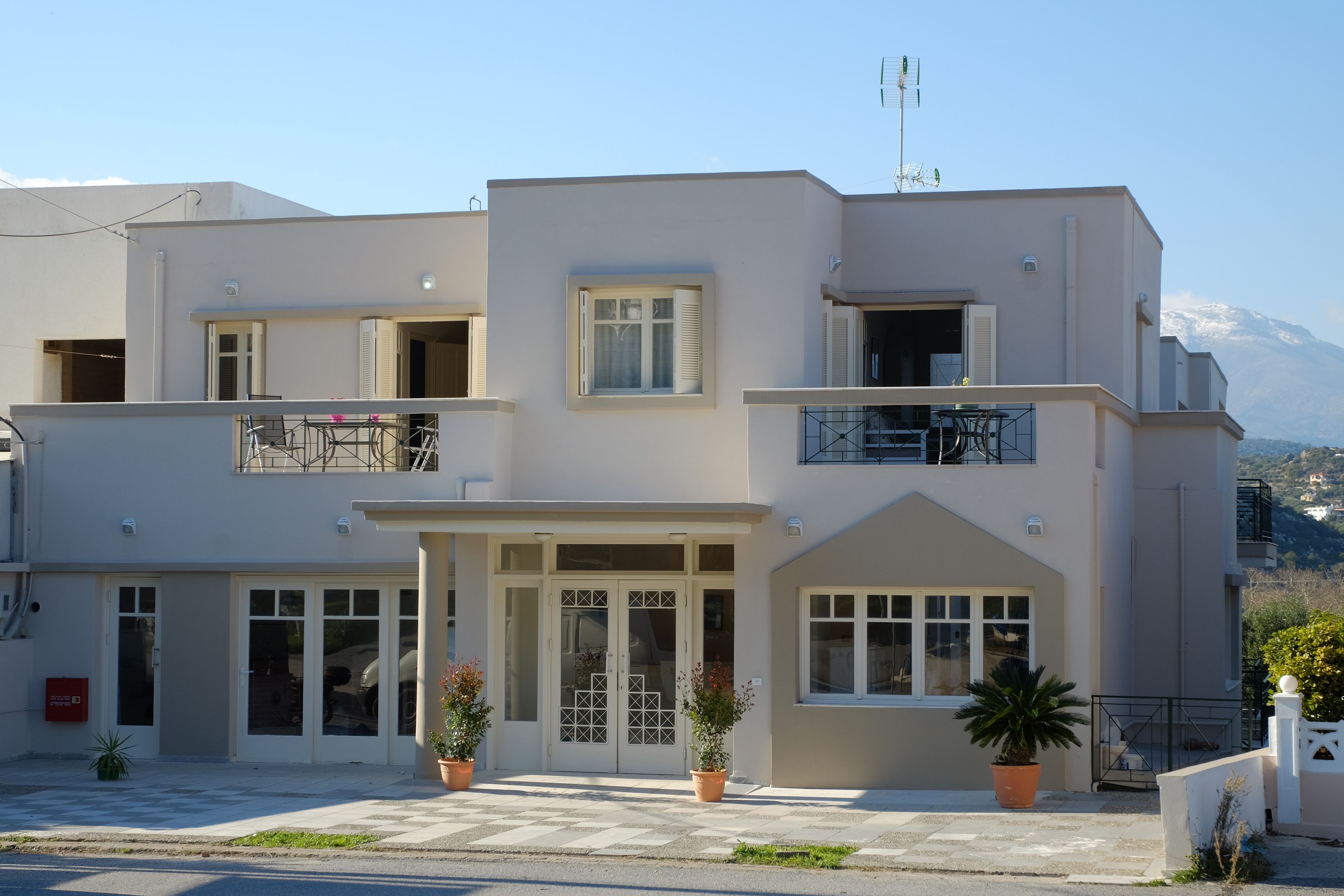 A two-story building with a balcony, large windows, and a mountain in the background.