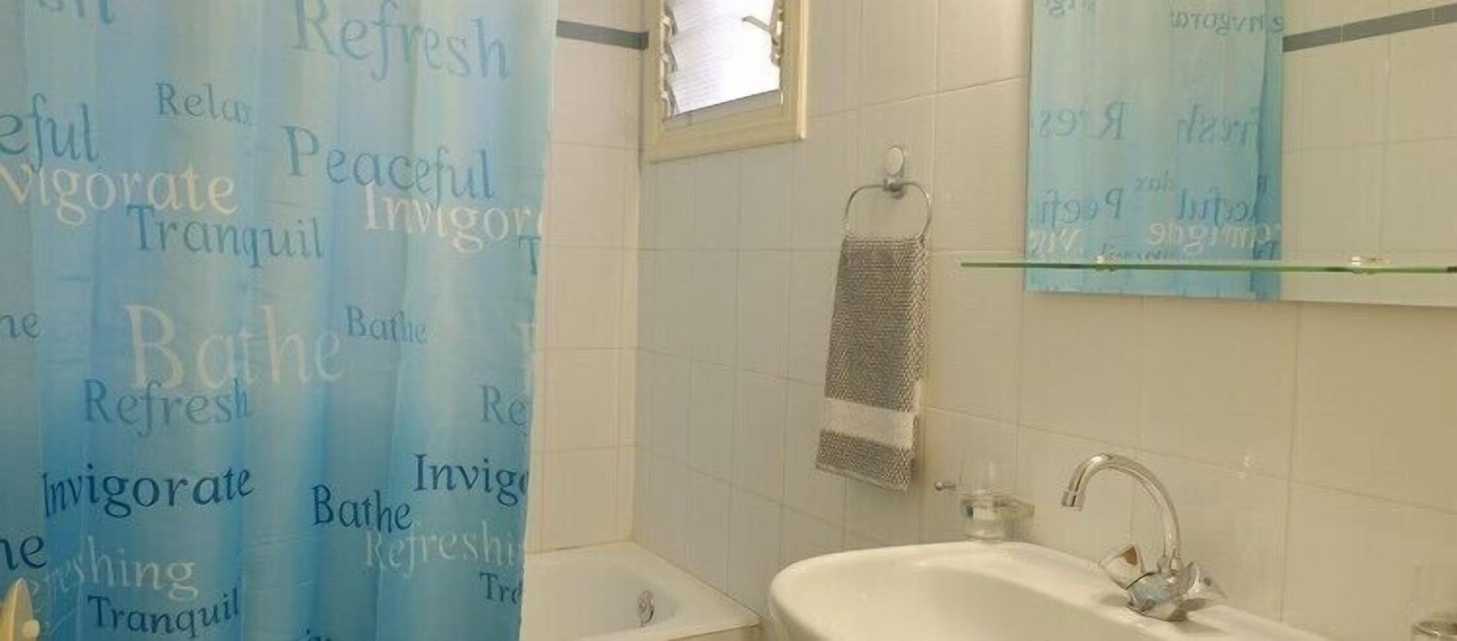 A bathroom with a shower curtain featuring words like 'Refresh' and 'Invigorate'. There is a towel rack with a towel, a sink, and a mirror above it.
