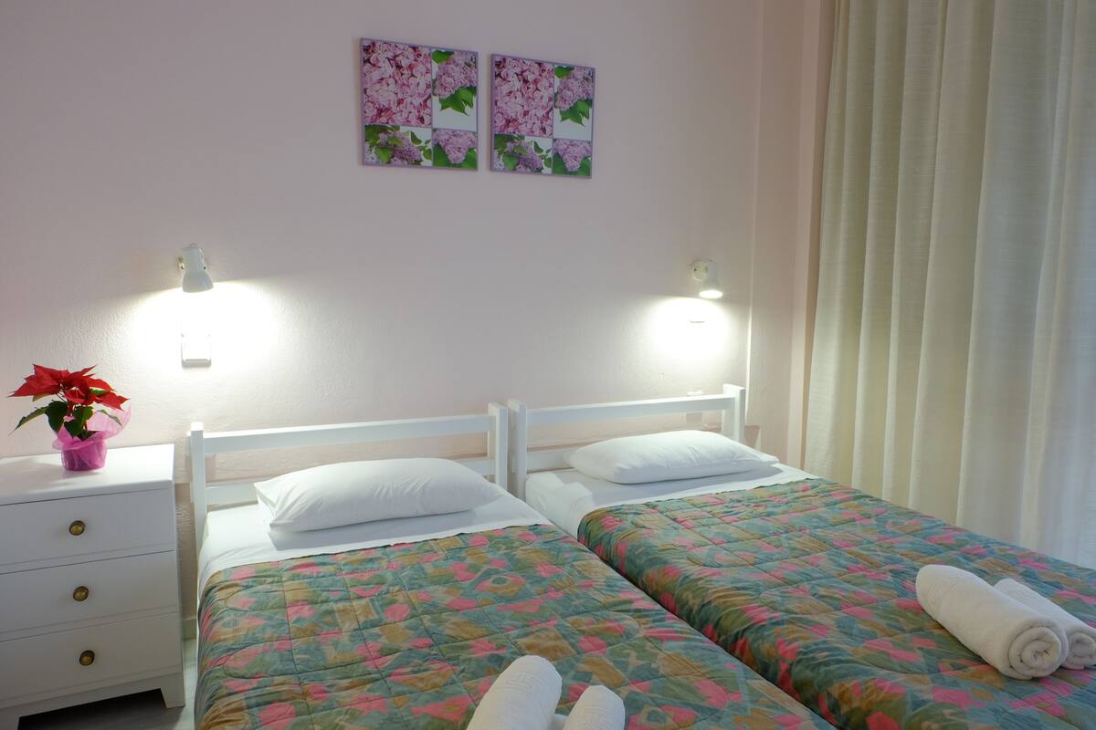 A double bed with floral bedding, a bedside table with a plant, and two wall-mounted lamps.