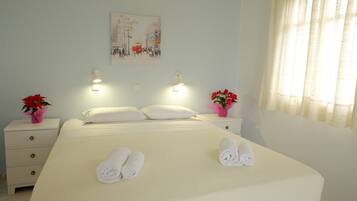 A neatly made bed with rolled towels, a painting on the wall, and two bedside tables with lamps and flowers.