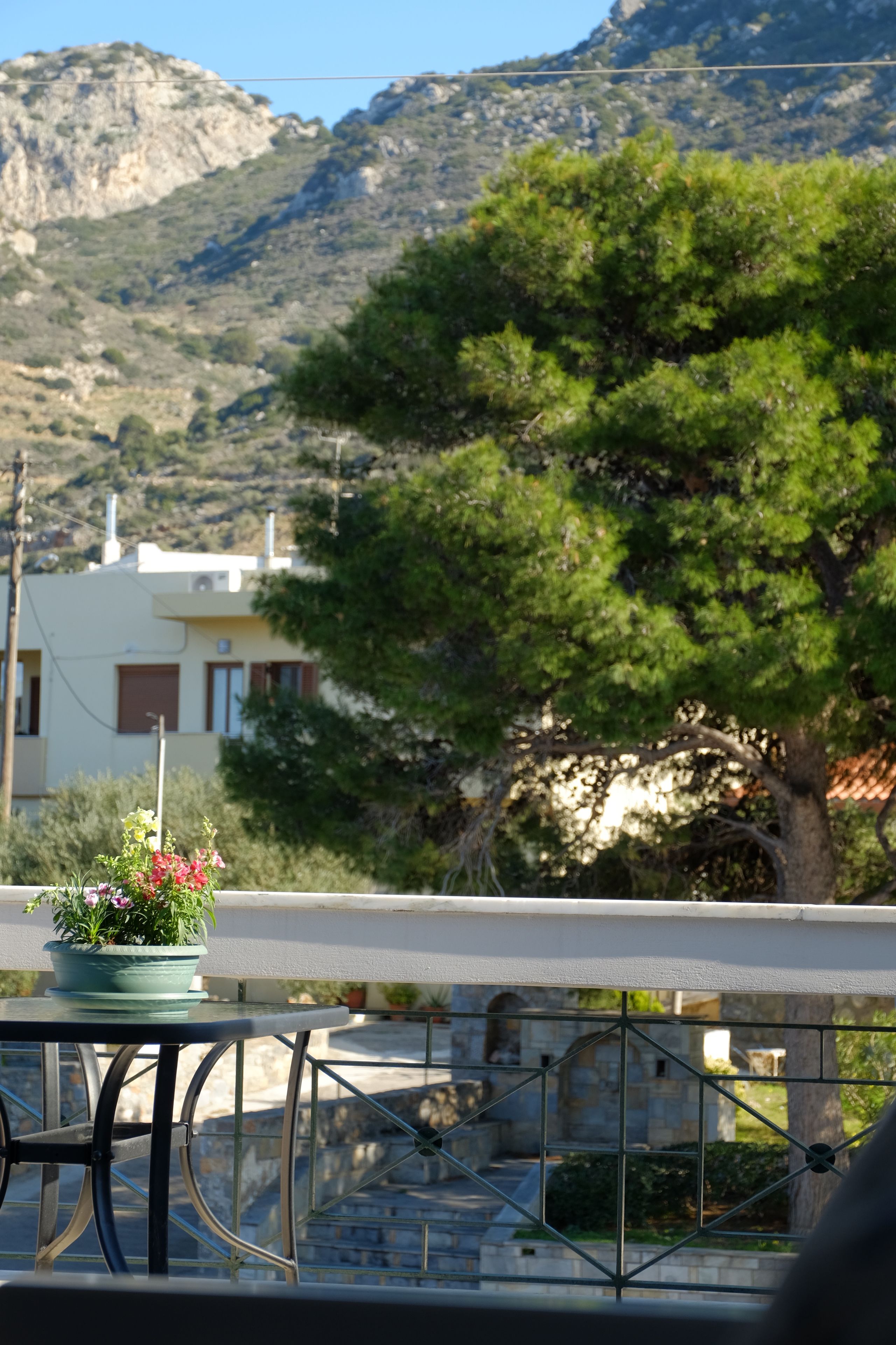 Una terraza con una mesa y sillas, una planta en maceta y una vista de una montaña y un edificio al fondo.