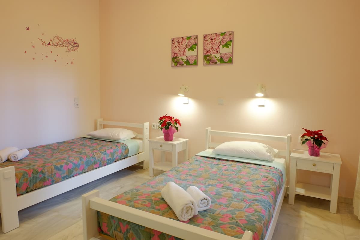 Two single beds with floral bedding, bedside tables with lamps, and decorative wall art.