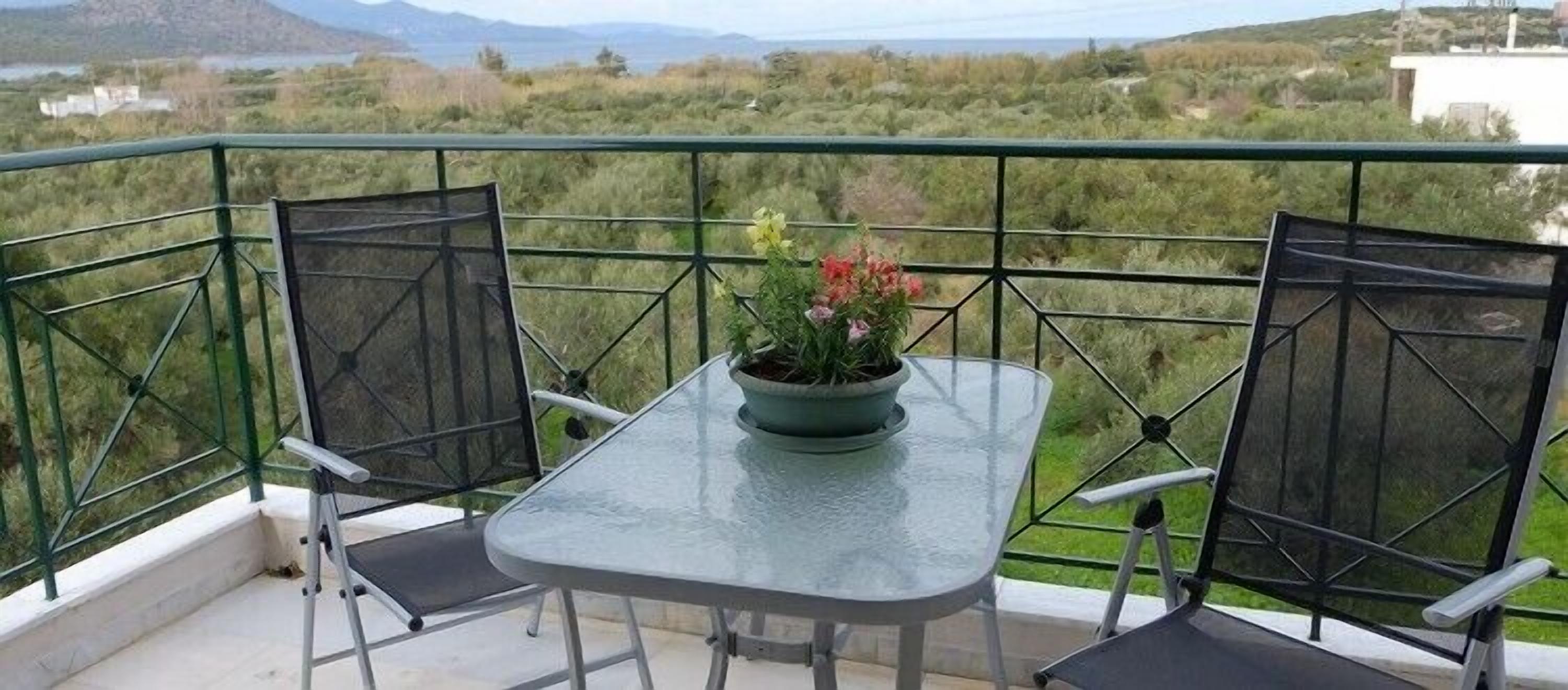 A balcony with a table and two chairs, a potted plant, and a view of a natural landscape.