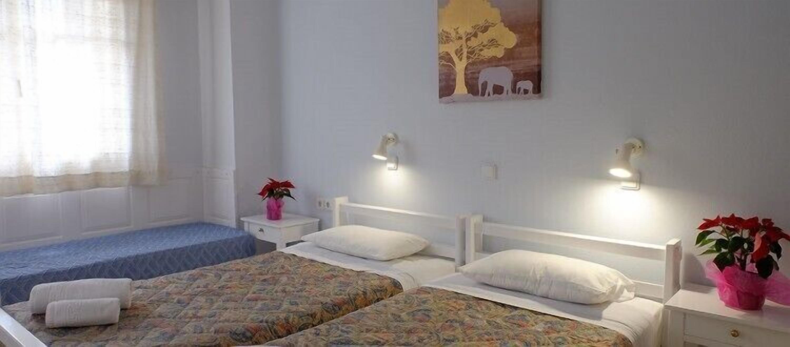 A bedroom with two beds, a small bedside table with a lamp, a window with curtains, and a wall painting.
