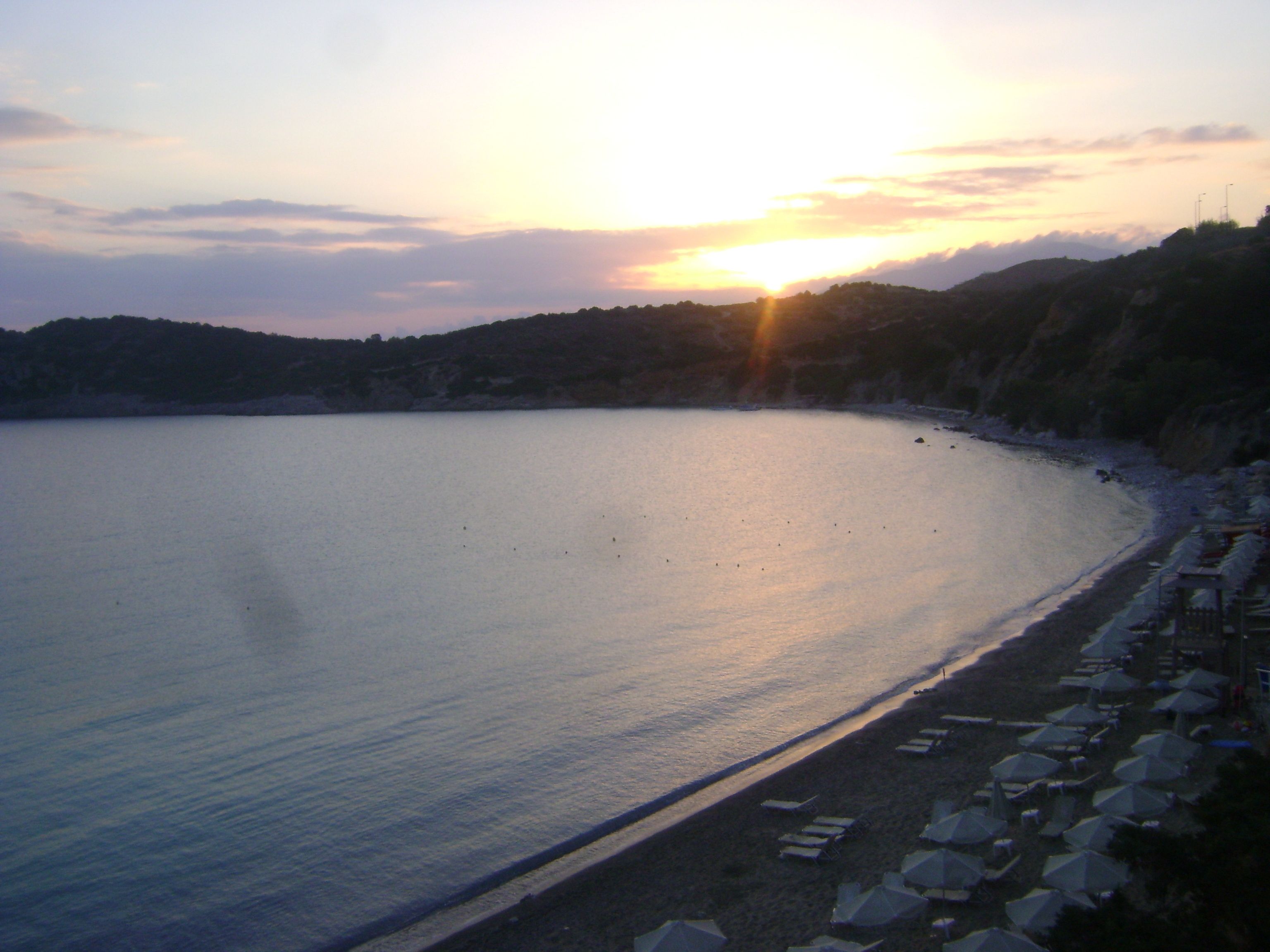 A beach with a row of umbrellas and lounge chairs along the shoreline.