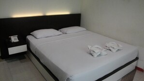 A neatly made bed with white linens and pillows, a bedside phone, and a pair of towels on the bed. - Hotel Pagi (Labuan Bajo)