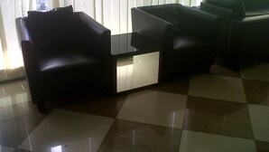 A modern living room with a black leather sofa, a glass coffee table, and a checkered floor. - Hotel Pagi (Labuan Bajo)