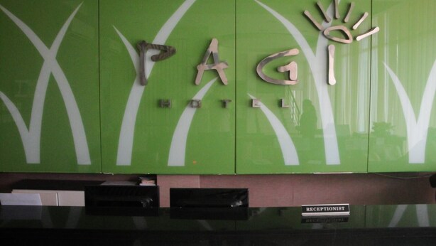 A reception area with a green wall displaying the letters "PAG" and a hand symbol, indicating a hotel. - Hotel Pagi (Labuan Bajo)
