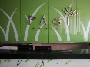 Ein Empfangsbereich mit einer grünen Wand, die die Buchstaben „PAG“ und ein Handsymbol zeigt, erkennbar als Hotel.