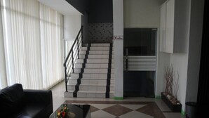 A modern living room with a black leather sofa, a glass coffee table with a floral centerpiece, a staircase with a black railing, and a 'No Smoking' sign. - Hotel Pagi (Labuan Bajo)