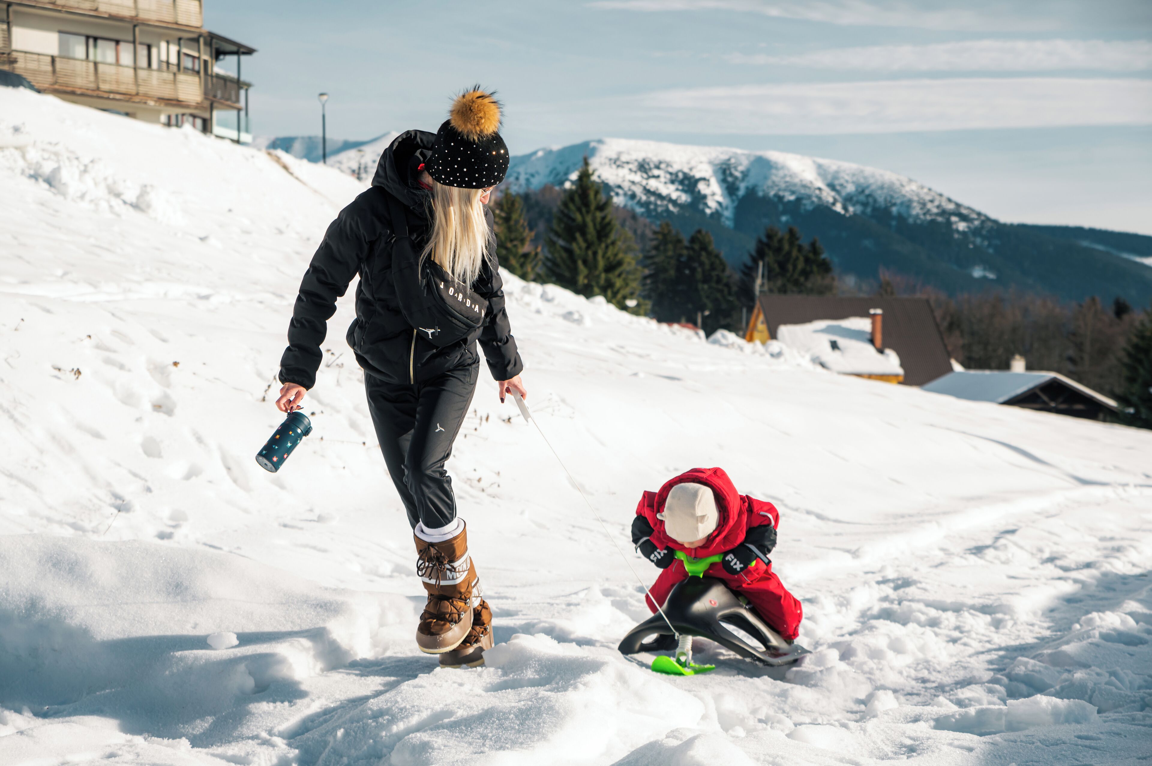 A snowy landscape with a person in a black jacket and a child in a red jacket.