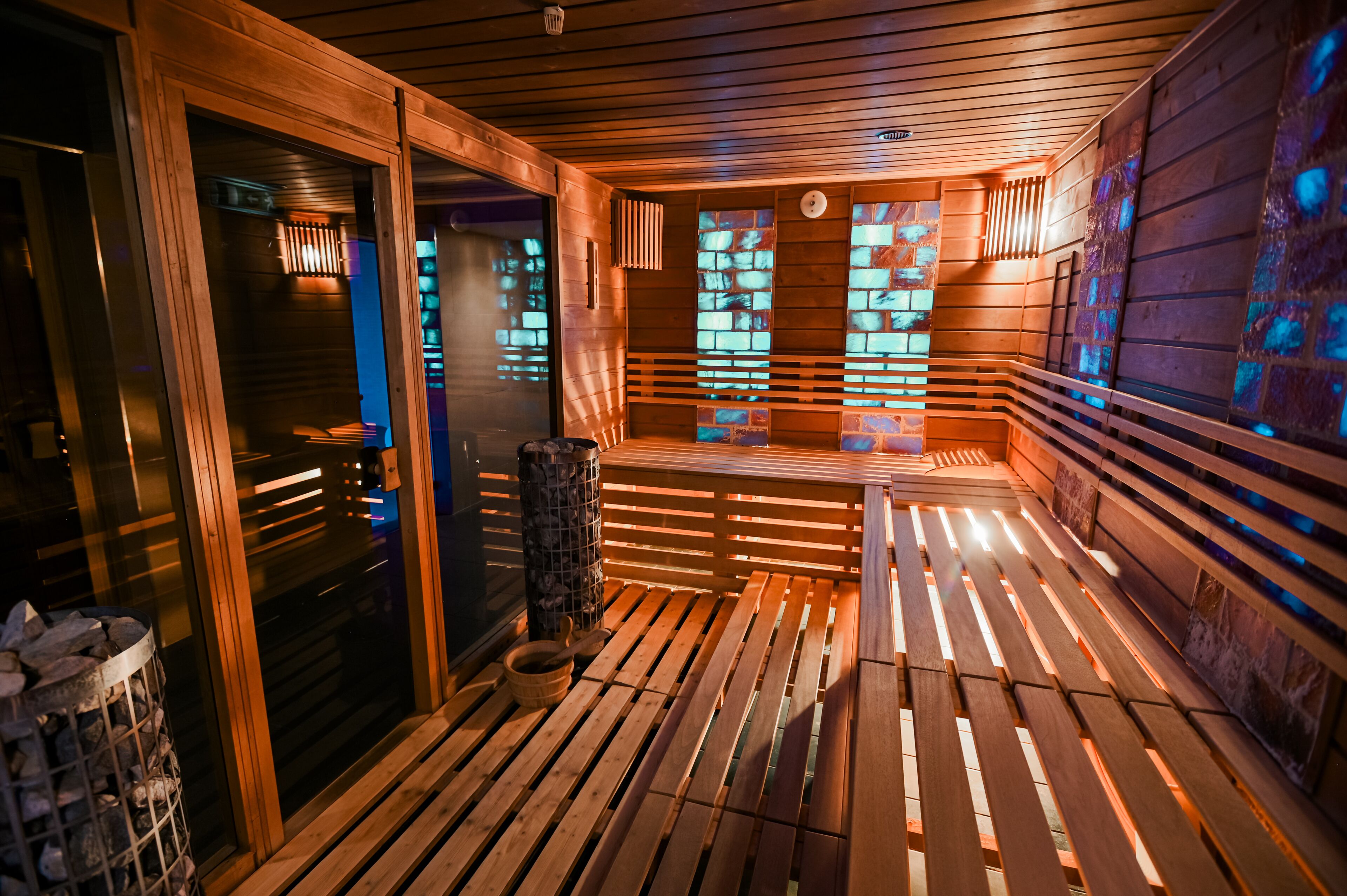 Una sauna con bancos de madera y piso de baldosas, que incluye una puerta de cristal y una pared de piedra.