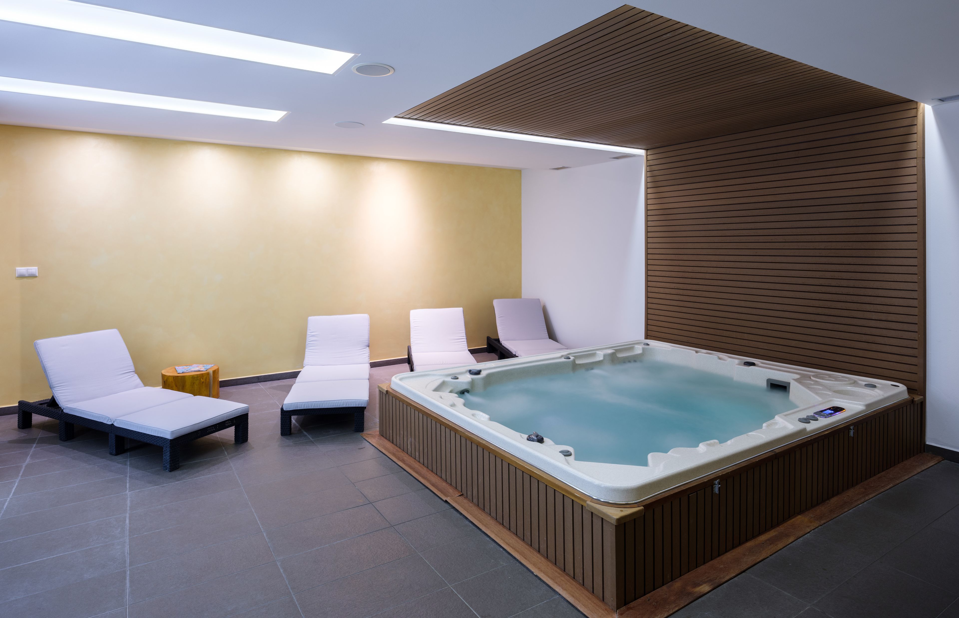 A spa room with a hot tub, four white lounge chairs, and a wooden wall panel.
