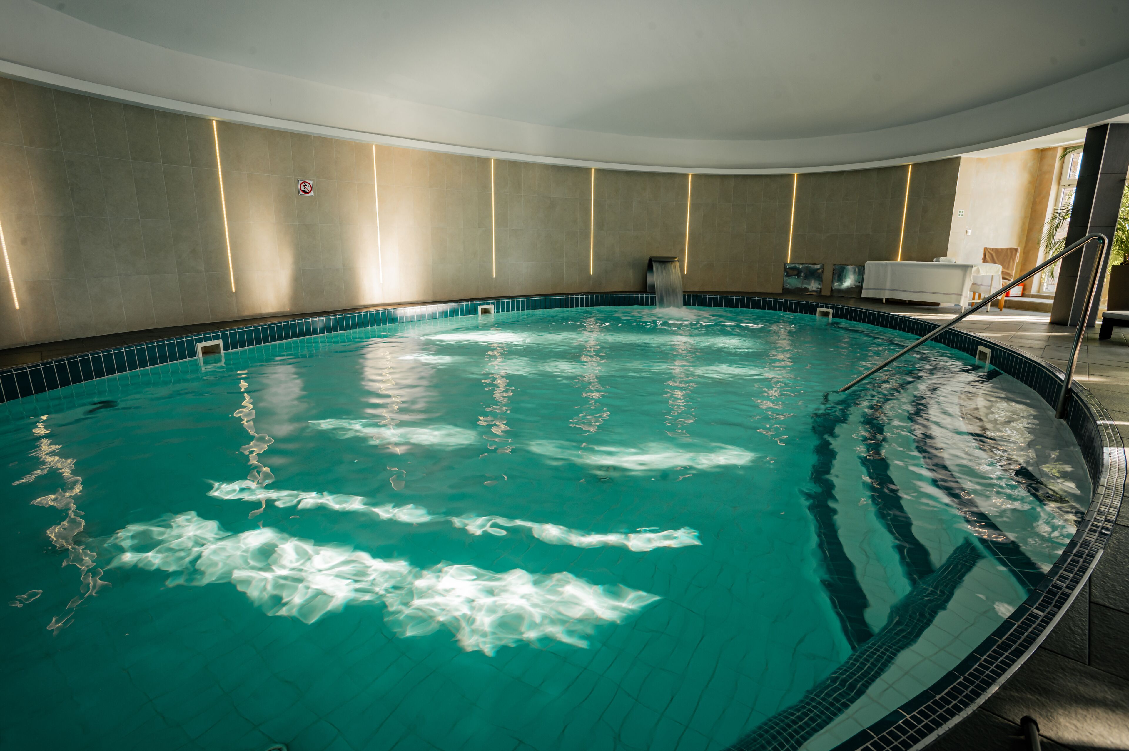 A large indoor swimming pool with clear water, surrounded by a tiled deck and a curved wall.