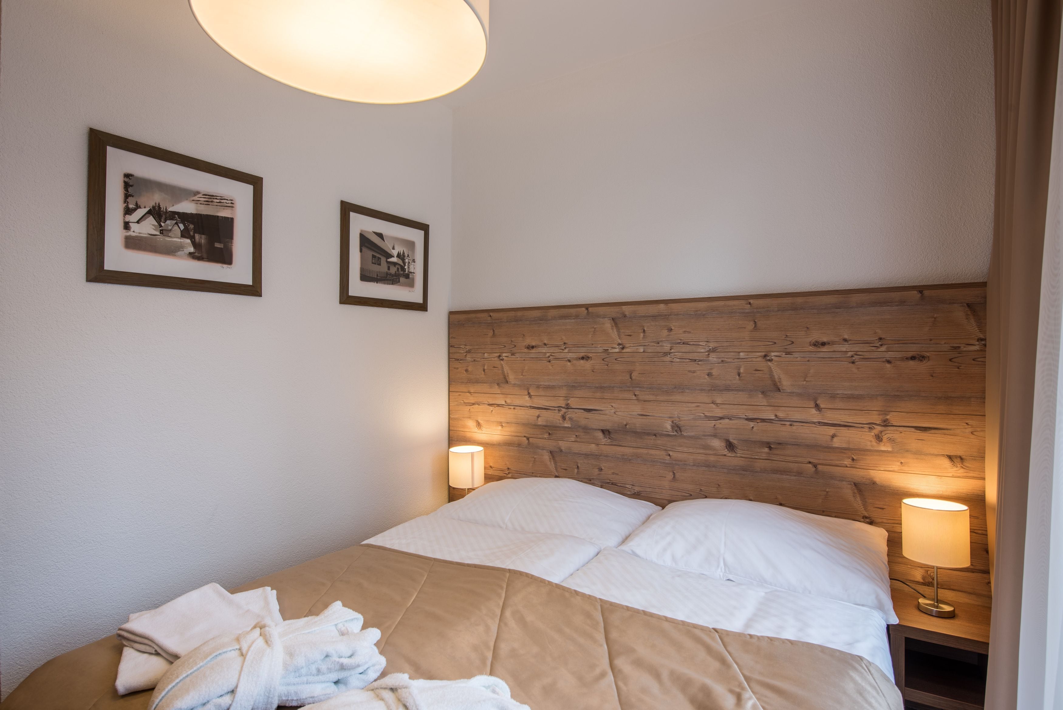 Een netjes opgemaakt bed met een houten hoofdbord, twee bedlampen en twee ingelijste foto's aan de muur.