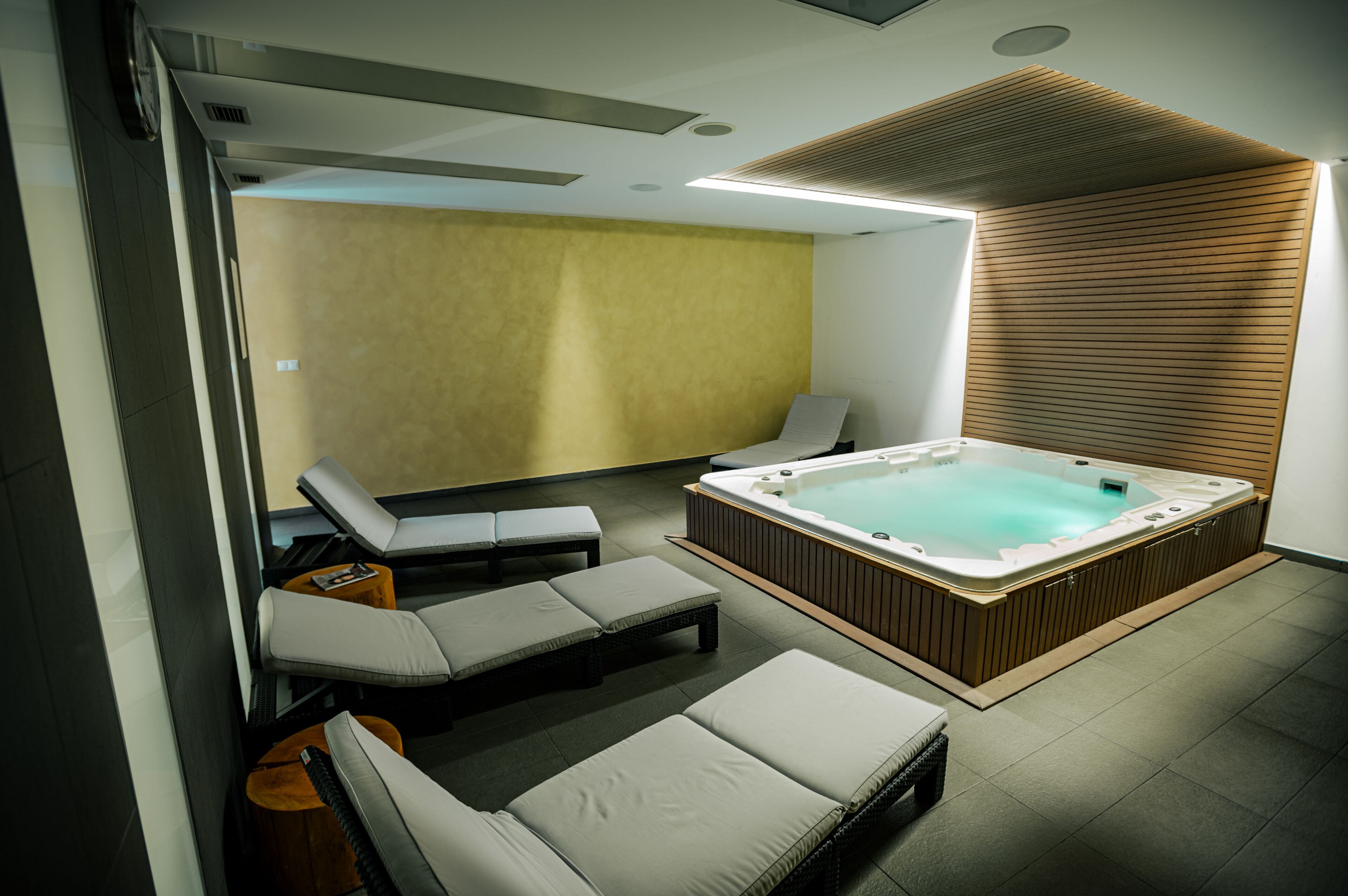 A modern spa area with a hot tub, lounge chairs, and a wooden wall.