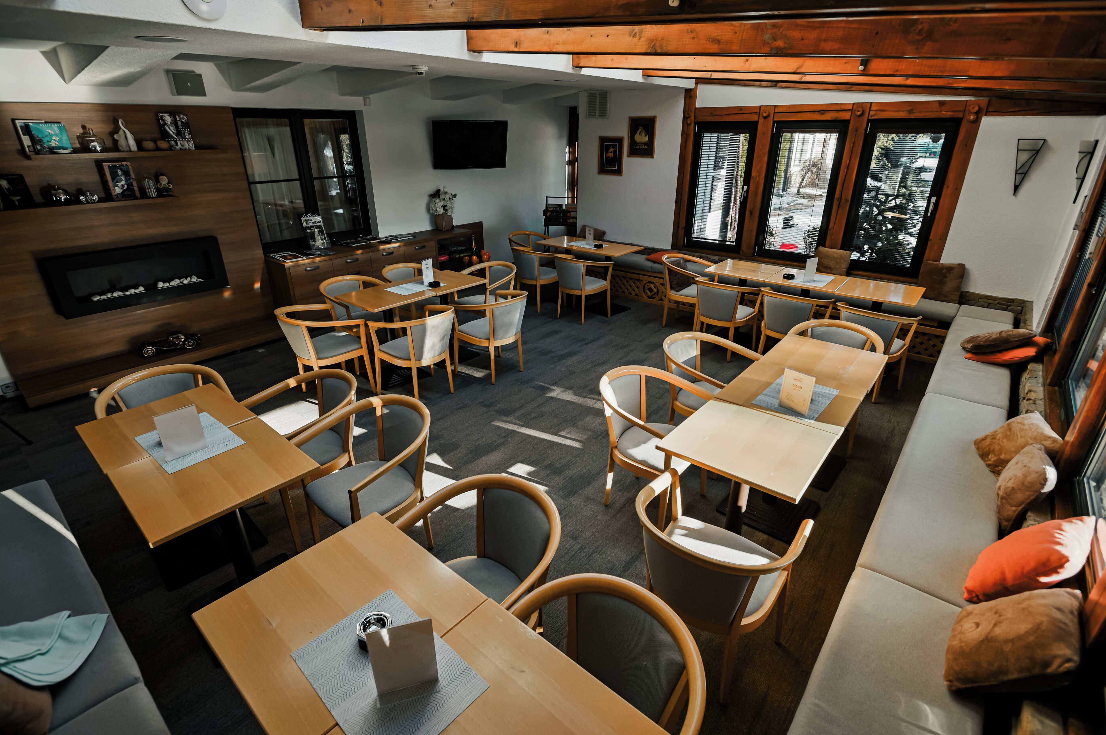 Un restaurante acogedor con mesas y sillas de madera, una chimenea y grandes ventanales con vistas al exterior.