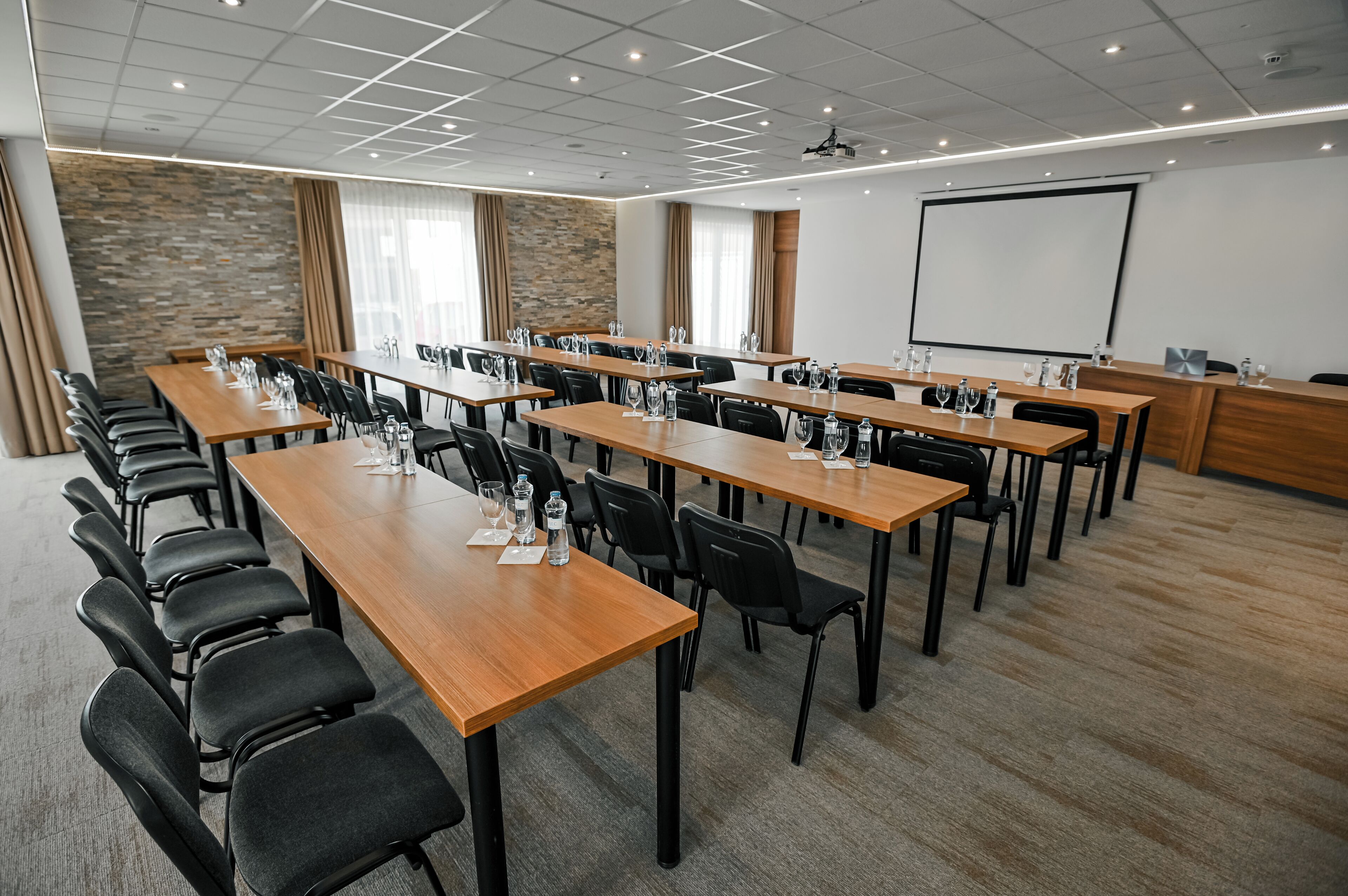 A conference room with long tables, chairs, and a projector screen.