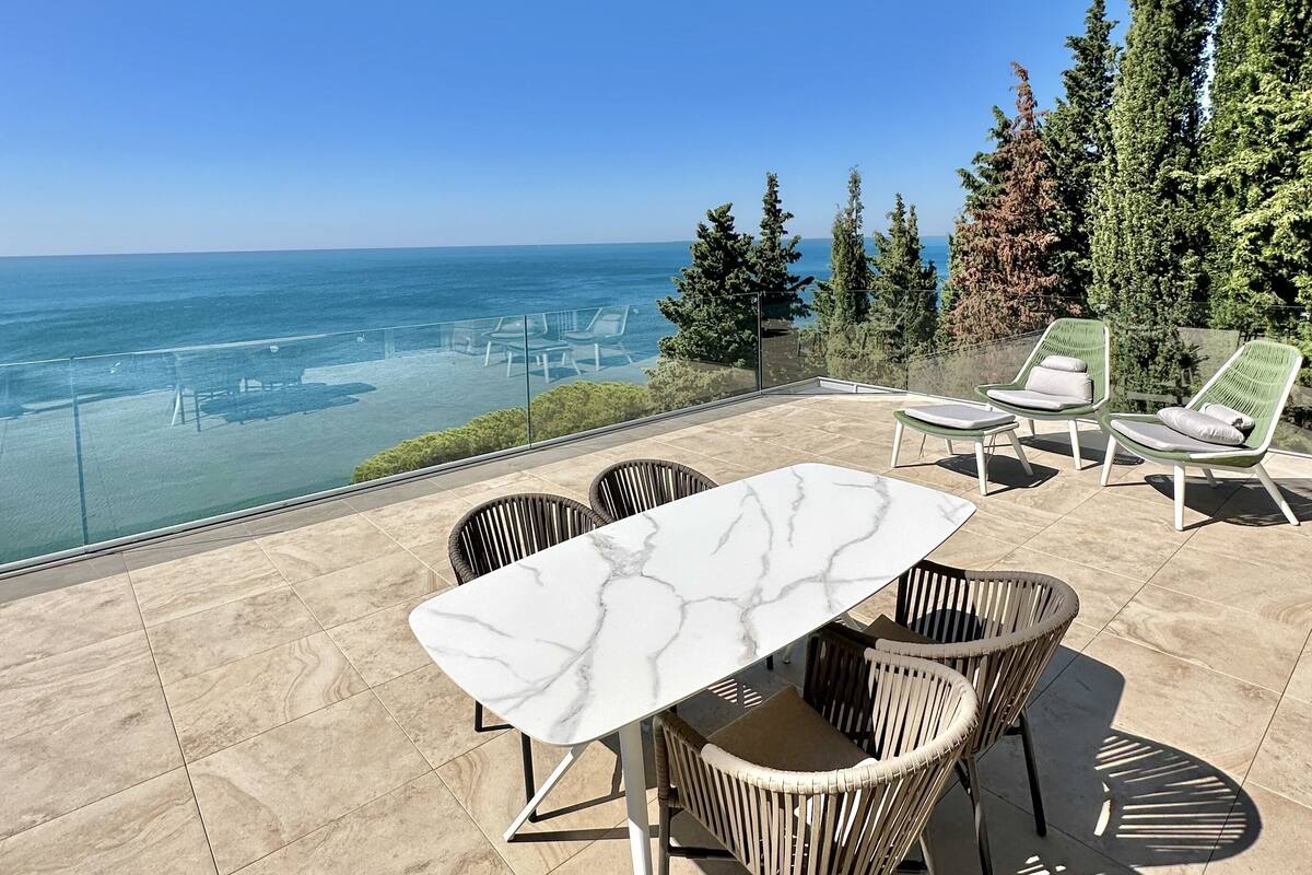 Une terrasse avec une table en marbre et des chaises en osier, donnant sur une étendue d’eau et une végétation luxuriante.