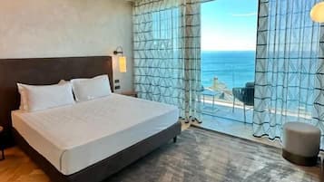 Habitación de hotel con cama, vista al mar y un ventanal grande con cortinas.