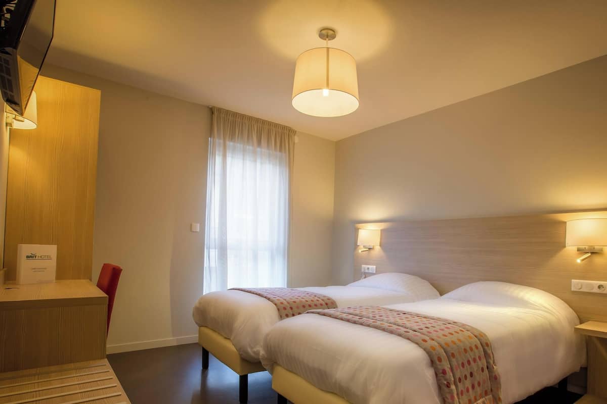 Une chambre d’hôtel avec un lit, des lampes de chevet, un bureau et une fenêtre avec des rideaux.