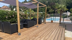 An outdoor wooden deck with black wicker furniture and a pool in the background.