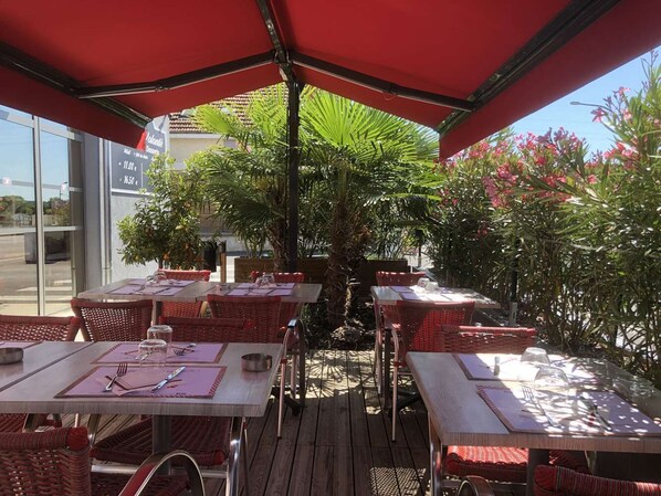 An outdoor dining area with tables and chairs, a central palm tree, and a red umbrella. - Brit Hotel Brive (Malemort-sur-Correze)