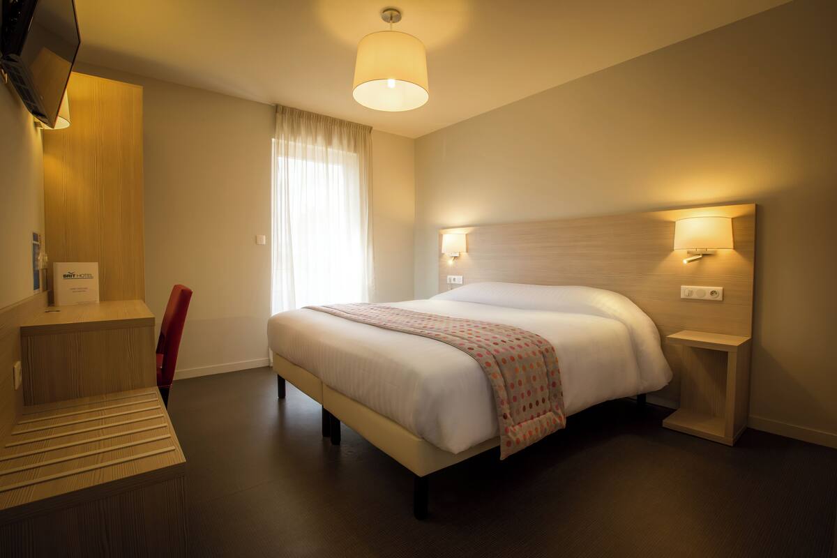 Une chambre d’hôtel comprenant un lit, des lampes de chevet, une télévision et un bureau avec une chaise.
