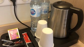A hotel room's minibar with a kettle, two water bottles, a cup, a tray with napkins, a book, and some snacks.