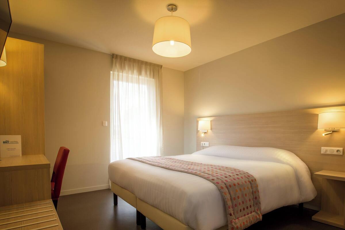 Une chambre d’hôtel avec un lit, des lampes de chevet, un bureau et un téléviseur.