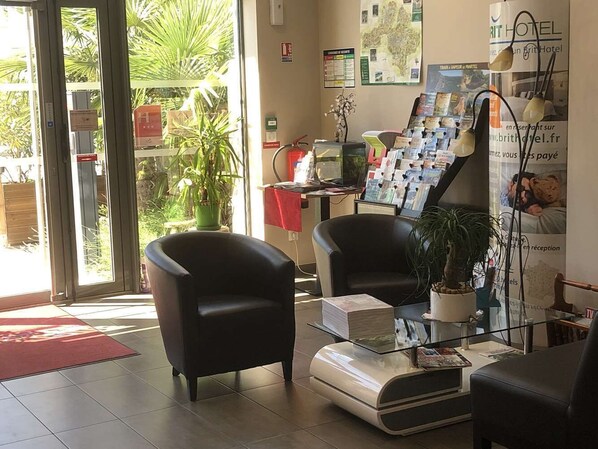 Un área de recepción con dos sillones de cuero negro, un mostrador de recepción con folletos, una planta en maceta y una mesa de centro de vidrio.