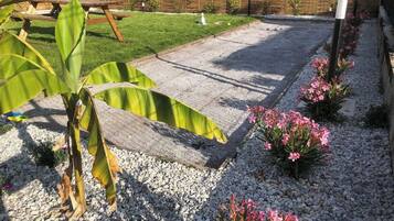 Een tuin met een betonnen terras, grindpaden en bloeiende planten.