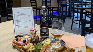 A restaurant setting with a menu, a bottle of wine, a glass of beer, and a variety of appetizers on a wooden board.