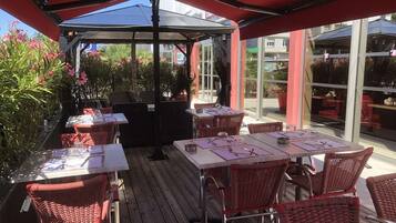 An outdoor patio area with tables and wicker chairs, covered by a red canopy.