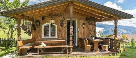 A rustic wooden building with a covered patio, benches, and a table.