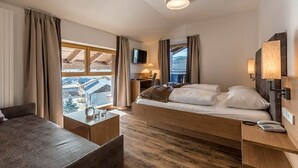 A hotel room with a bed, bedside table, lamp, and a TV. - Hotel Alpenfrieden (Rio di Pusteria)