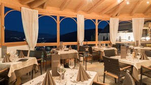 A restaurant with multiple tables set for dining, featuring a view of the mountains at dusk. - Hotel Alpenfrieden (Rio di Pusteria)