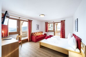 Ett hotellrum med en säng, ett skrivbord, en stol, en soffa och stora fönster med gardiner.