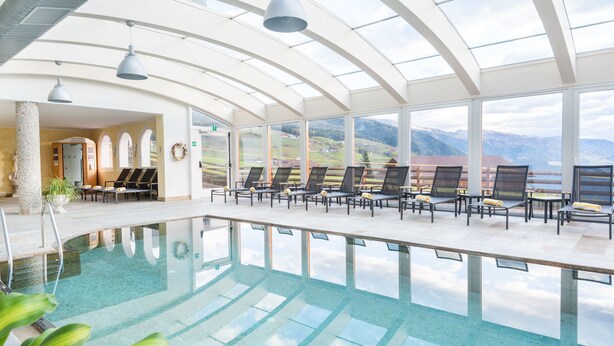 An indoor swimming pool with lounge chairs and a view of mountains. - Hotel Alpenfrieden (Rio di Pusteria)