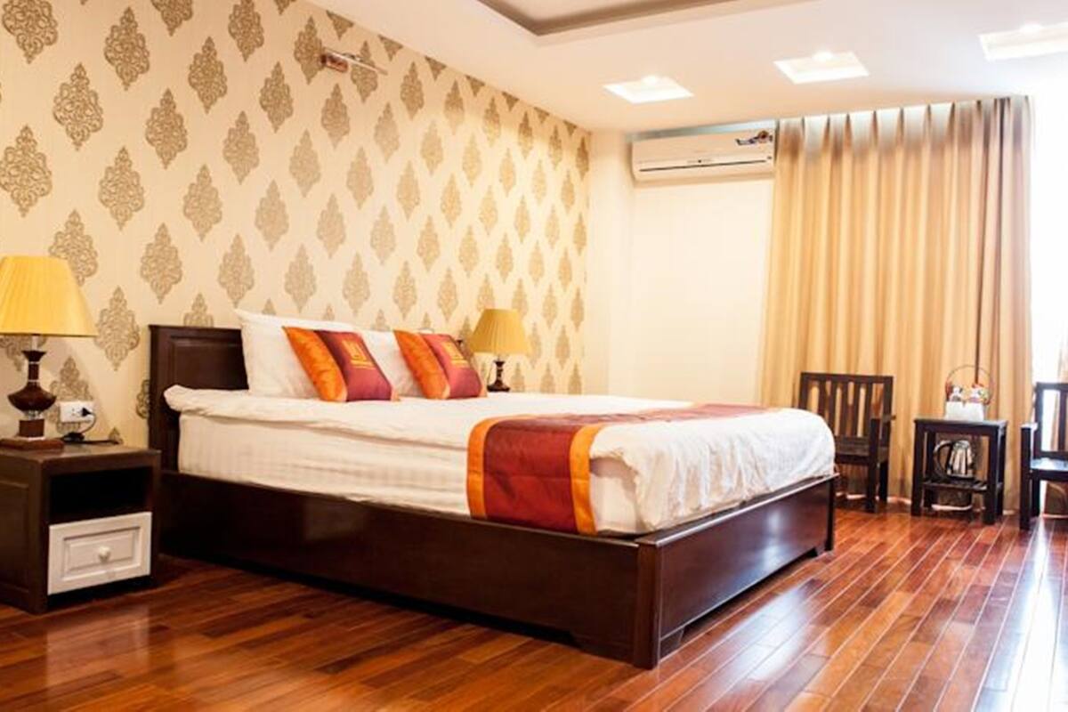 A hotel room with a large bed, two bedside lamps, a wooden nightstand, a chair, and a small table with a lamp.