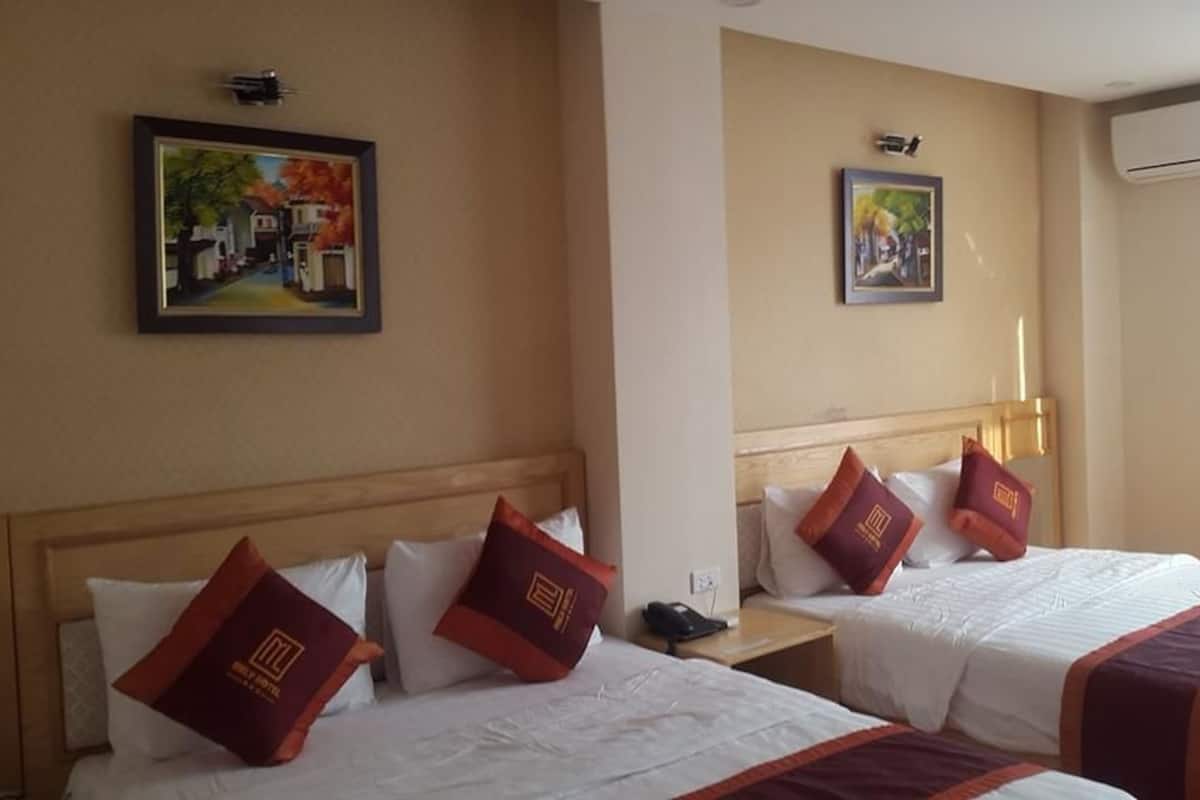 A hotel room with two beds, each with white bedding and maroon pillows. There are wall-mounted air conditioning units and framed artwork above the beds.